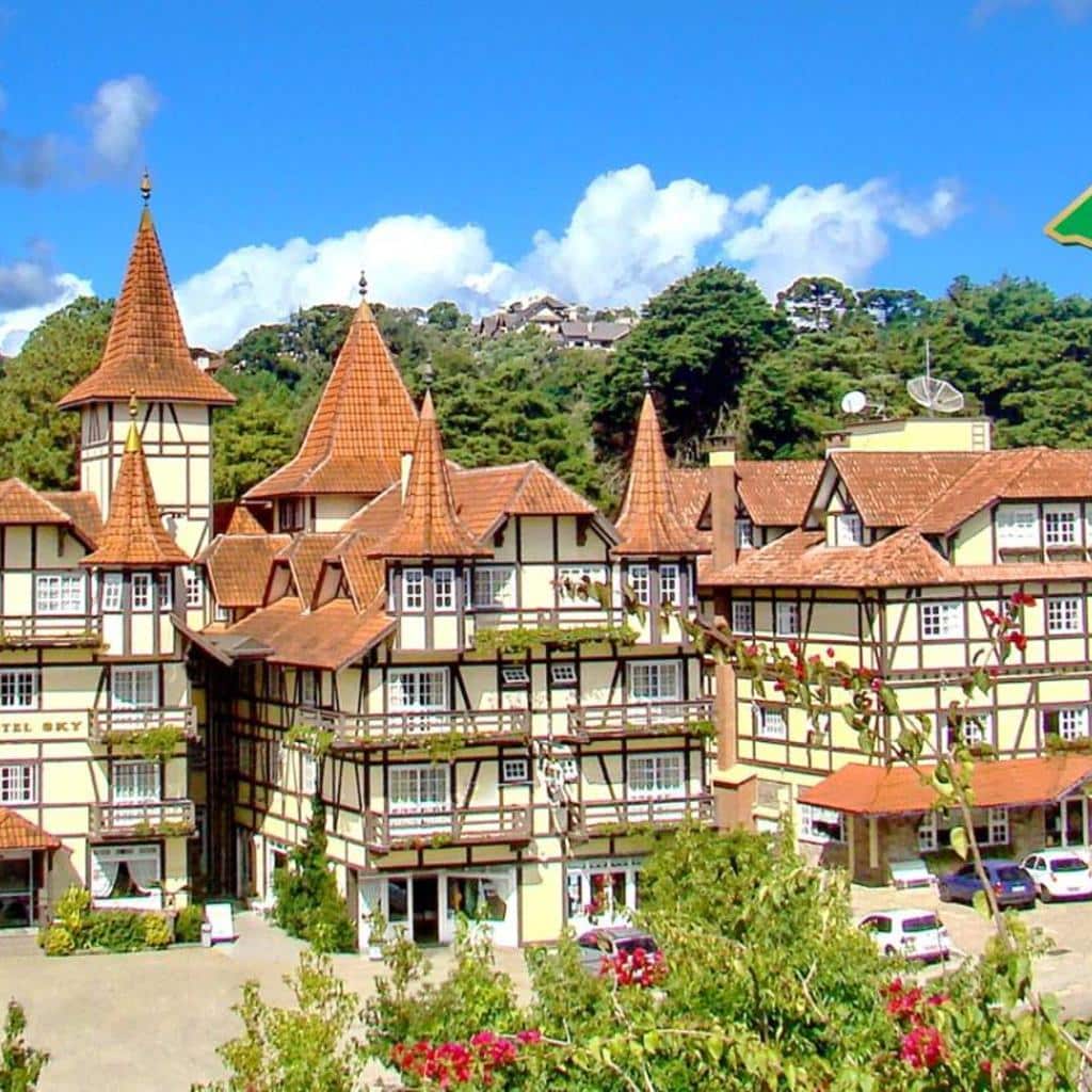O Hotel Sky Gramado, com telhados íngremes e pontiagudos e paredes em estilo enxaimel, está situado entre as árvores e o céu azul.