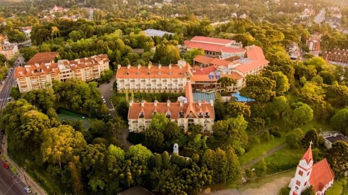 Vista aérea dos edifícios com telhados vermelhos do Wish Serrano Resort, aninhados entre árvores e vegetação em uma área ensolarada e panorâmica.